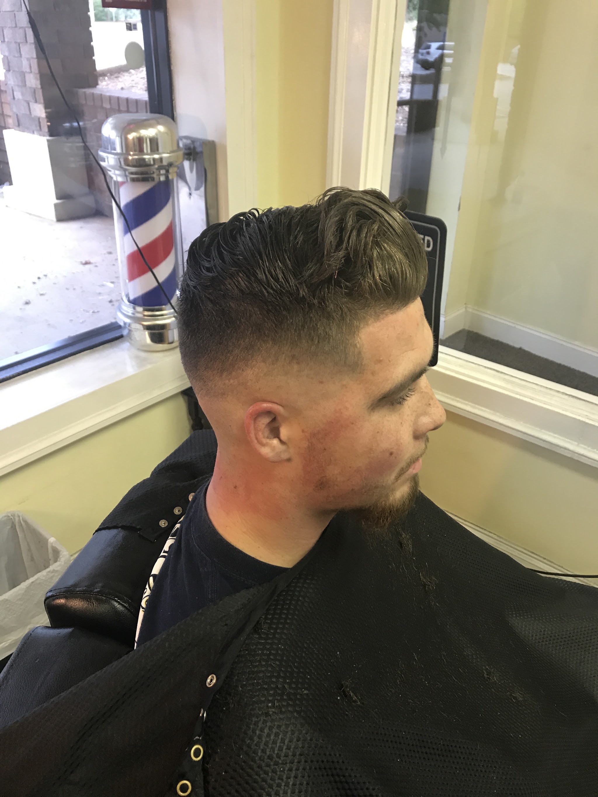 A fade with a styled top, barber pole behind